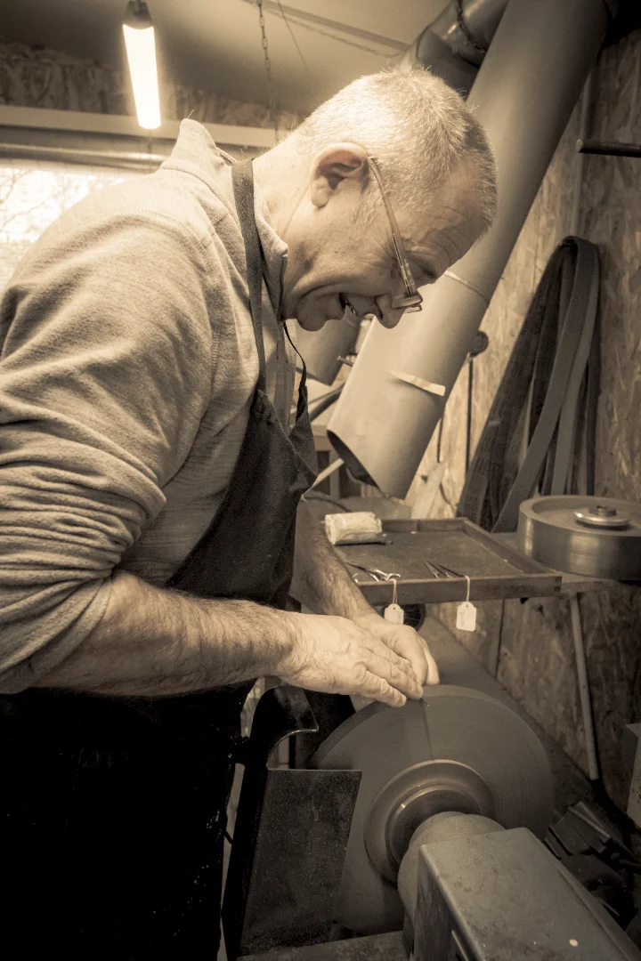 Christian Jouteau assurant la passation avec Robert, travaillant dans l'atelier d'affûtage sur une meule.