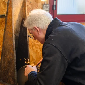 John concentré sur son action, affutant avec précision un peigne de tondeuse sur une meule circulaire.
