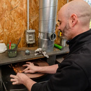 William en train d'affûter un peigne de tondeuse sur une meule, créant des étincelles.